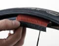 Trennen Sie mit Schere oder Seitenschneider ein gut fünf Zentimeter langes Stück aus einem alten Reifen heraus, schneiden Sie die Reifenkerne so knapp wie möglich ab. Damit die Einlage möglichst wenig aufträgt, sollte die Gummilauffläche entfernt werden. Dies gelingt mit einer Raspel oder einfacher mit einem Bandschleifer mit grobem Schmirgelleinen. Wichtig: Montieren Sie den reparierten Reifen zu Ihrer Sicherheit auf das Hinterrad.