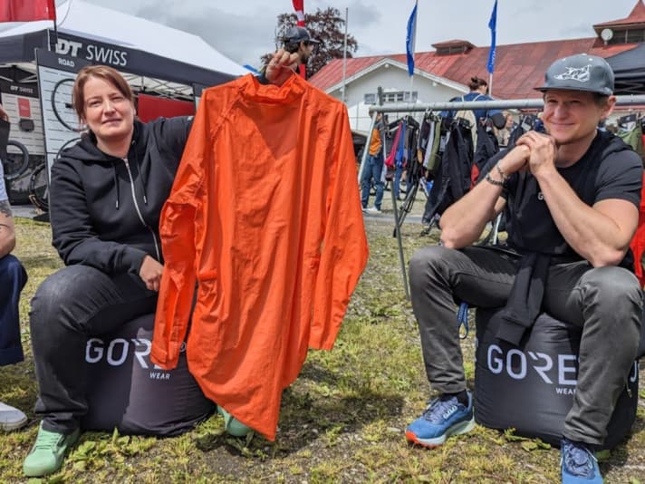 Claudia Leiner, Marketing-Managerin bei Gore Wear, zeigt die erste fahrradspezifische Regenjacke. Rechts davon sitzt Michael Jean-Jacques, Produktmanagement.