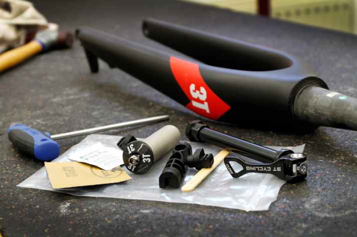   Die 3T Rigid Carbon-Gabel und das mitgelieferte Zubehör: Steckachse, 3T-Steuersatzkappe und Gabelschafteinsatz zum Einkleben. Schleifpapier, Alkoholtupfer sowie der Epoxidharzkleber (nicht im Bild) sind gleich mit dabei – und ein Eisstäbchen zum Verschmieren.