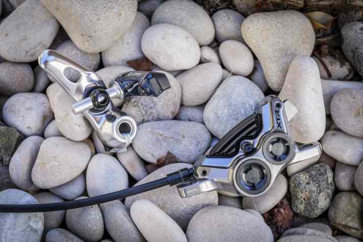 Welche dieser Shimano Bremsen hat wohl mehr Bremspower? Die Felgenbremse von 1982 ist es sicher nicht. Die neue XTR Vierkolben-Scheibenbremse ist dagegen ein richtiger Anker.
