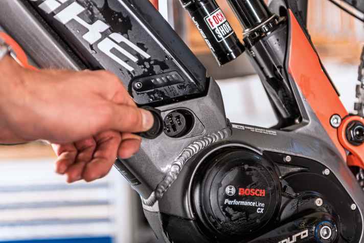    4 Lade-Port: Bei allen E-MTBs sind die On-Board-Lade-Ports der Akkus mit Abdeckungen versehen. Bei der Reinigung des Bikes sollten Sie darauf achten, dass die Abdeckungen geschlossen sind. Kommt doch einmal Wasser dran und schlimmstenfalls auf die Kontakte, entnehmen Sie den Akku, tupfen Sie die Feuchtigkeit ab und lassen das Bike in der Sonne trocknen. Grundsätzlich sind die Bikes spritzwasserfest gedichtet. Wenn der Lade- Port zu ist, kann also auch beim Durchfahren einer Pfütze oder bei einem Regenguss nichts passieren. Es empfiehlt sich allerdings, die Kontakte einmal im Jahr mit Kontaktfett (im Elektronik-Zubehörhandel erhältlich) zu pflegen.    
