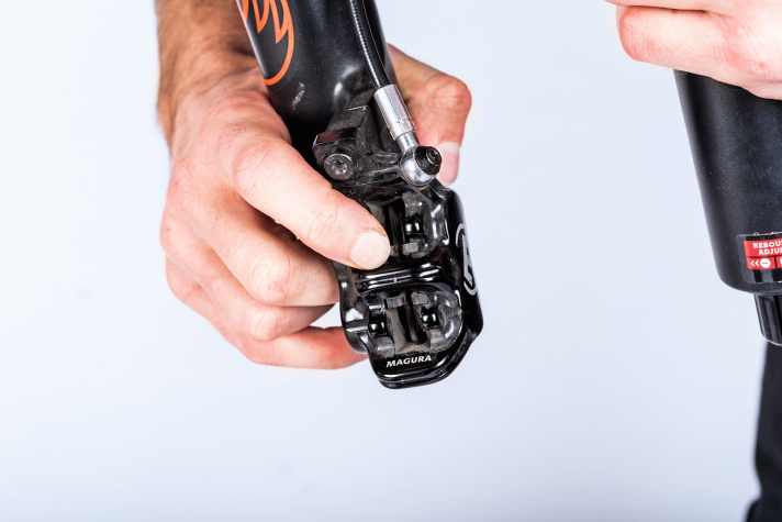    2 Bremsbeläge herausdrücken: Lösen Sie die Sicherungsschraube.Drücken Sie von der Rückseite des Bremssattels auf die kleinen Haltenasen der Beläge, schieben Sie jetzt die Beläge nach hinten durch, sodass die Haltenasen am Brems-sattel vorbeikommen. 