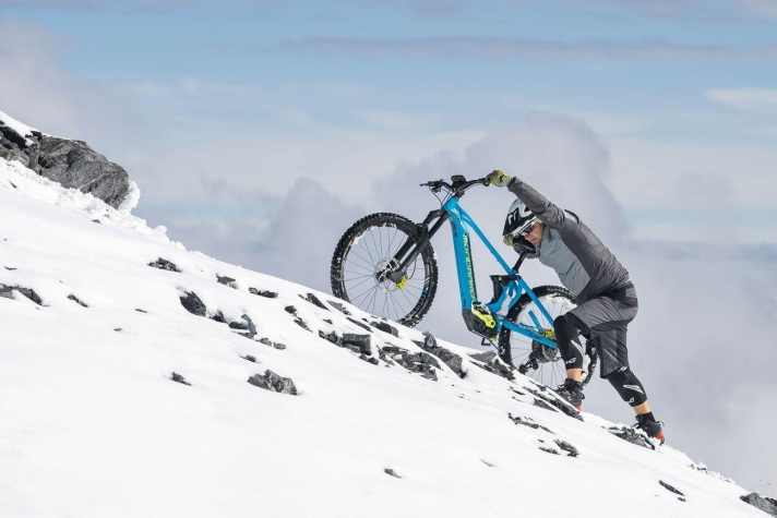   SCHIEBEHILFE WIRKSAM EINSETZEN – Die Unterstützung eröffnet uns vor allem im Winter neues Terrain. Steile Anstiege, die mit dem klassischen Bike schlicht nicht möglich sind, lassen sich mit dem E-MTB spielend bewerkstelligen. Doch irgendwann zeigt uns die Physik auch hier die Grenzen auf. Wenn das Hinterrad durchdreht, hilft nur noch Schieben. Die neuen, wirkungsvollen Schiebehilfen nehmen steilen Anstiegen im Schnee den Schrecken. Wer es versteht, sie wirkungsvoll einzusetzen, kommt sogar kraftsparender voran als per pedes. Der Trick ist auch hier, möglichst viel Druck aufs Hinterrad zu bringen. Versenken Sie zunächst den Sattel. Pressen Sie jetzt Ihren Oberkörper auf den Sattel. So bringen Sie den Druck aufs Hinterrad. Je nach Steilheit können Sie jetzt die Schiebegeschwindigkeit über die Schaltung dosieren und mit der Hinterradbremse feinjustieren.