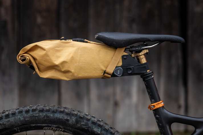 Boah, ey! Auch die neue Evoc-Satteltasche wird mit dem pfiffigen Dreh-Ratschen-Verschluss am Stützenrohr gehalten. Das Sattelgestell selbst umschlingen übliche Klettgurte. Auch die mit drei Litern Kapazität größte Variante ist mit den meisten Teleskopstützen kompatibel. Sie ragt zwar schnurstracks nach hinten, ist aber kompakt genug, sodass auch mit abgesenkter Stütze Luft für einfedernde Hinterräder bleibt (Foto).