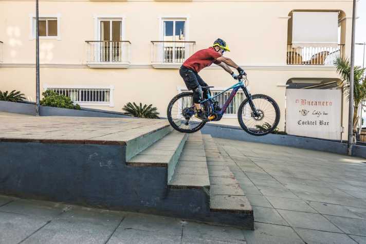   2. Sobald das Vorderrad an der ersten Stufe nach unten kippt, streckt man dynamisch Arme und Beine – so verlagert man das Körper­gewicht abrupt nach hinten, das Vorderrad wird entlastet. Das Bike rollt nun auf dem Hinterrad die Treppe hinunter. Bei der Landung verlagert man den Körper wieder nach vorne und federt den Impact mit Armen und Beinen ab.