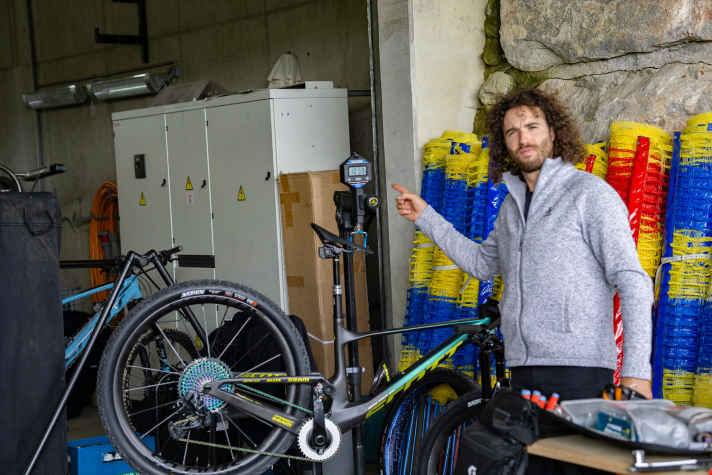   „Yanick the Mechanic“ ist Schurters persönlicher Mechaniker. Mit seiner akribischen Arbeit sorgt er dafür, dass Schurters Defektbilanz besser ist als bei den meisten Sportlern. Hier präsentiert er das neue Wettkampf-Bike von Nino an der Waage. Fahrfertige 10,59 Kilo wiegt das neue Arbeitsgerät von Schurter. Das Gewicht ist im Cross-Country-Racing nach wie vor wichtig, aber laut Aussage von Schurter und seinem Mechaniker nicht mehr die maßgebende Größe bei der Materialwahl. Je technischer die Strecken werden, desto wichtiger wird eine exzellente Funktion des Bikes. Und genau diese Exzellenz erhofft man sich von dem zusätzlichen Federweg, den breiten Reifen und der Teleskopstütze.