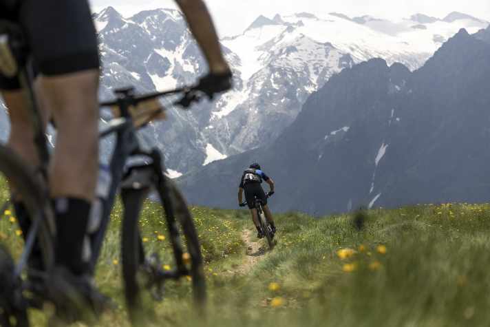 Maxxis BIKE Transalp 2024: vorne der Singletrail durch die Blumenwiese, hinten der Blick auf die Gletscher.