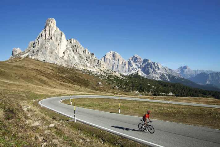 Radreise Dolomiten: Wie ein Fingerzeig erhebt sich die Ra Gusela (2595 m) über dem Passo di Giau (2236 m), rechts davon ragen die Gipfel der Tofane in den blauen Himmel.