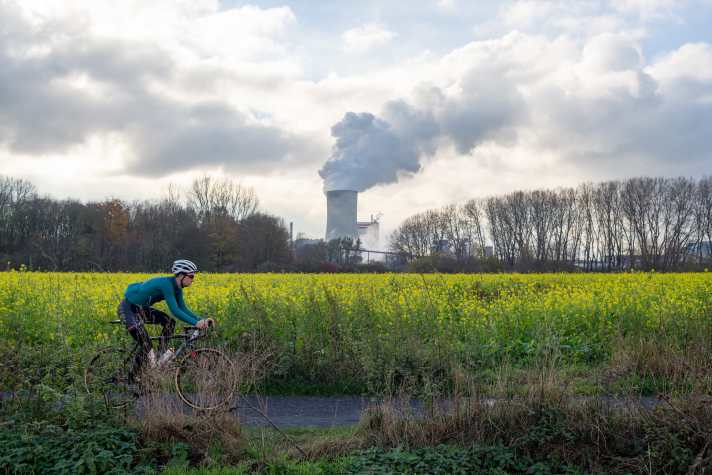 Joscha passiert ein Rapsfeld; im Hintergrund das Steinkohlekraftwerk von Trianel in Lünen