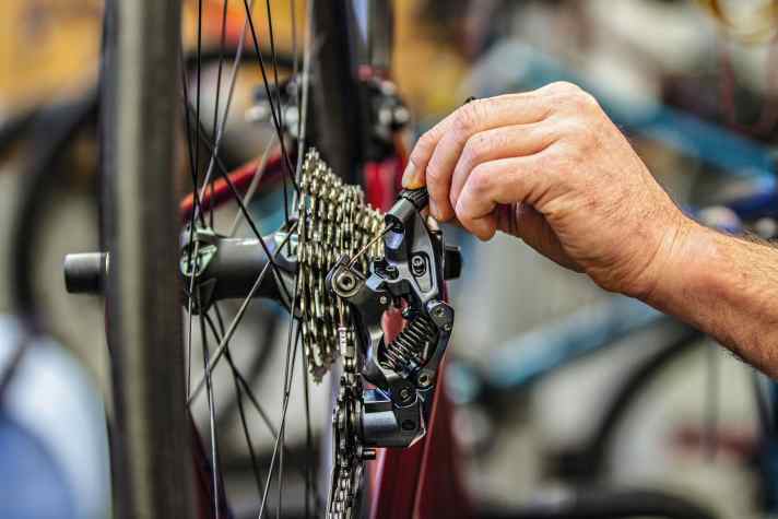 Drehen der Einstellschraube am Rennrad-Schaltwerk (im Bild Shimano) im Uhrzeigersinn verringert die Zugspannung, das Schaltwerk wandert nach außen bzw. rechts.