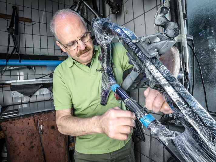 Bei einem Sturz hat ein Baumstumpf das Oberrohr perforiert. Der Rahmen ist zum Schutz vor Harz und Kratzern in Folie gepackt. Die Schadstelle wird per Klinge entlackt.