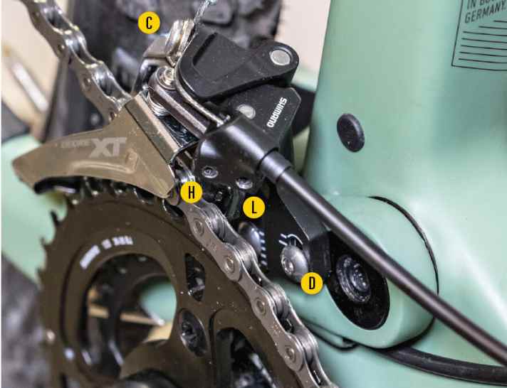   Ähnlich wie beim Schaltwerk hat der Umwerfer einer Shimano 2-fach Schaltung zwei Schrauben für den Anschlag (H, L). Schraube D lässt den Umwerfer in der richtigen Distanz zu Kette schweben, ähnlich wie die Umschlingungsschraube an der Schaltung. Und C arretiert lediglich den Schaltzug.