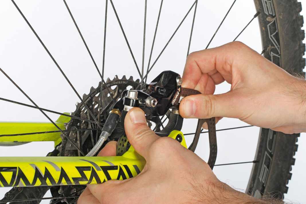 1. Der sogenannte Bremssattel-Reset ist an sich einfach, Sie müssen dazu noch nicht einmal das Laufrad ausbauen. Allerdings brauchen Sie einen Helfer. Als Erstes wird die Bremsscheibe kräftig auf einer Seite gegen den Bremsbelag gedrückt und in dieser Position gehalten. Das erfordert etwas Kraft, Handschuhe sind hierbei ratsam.