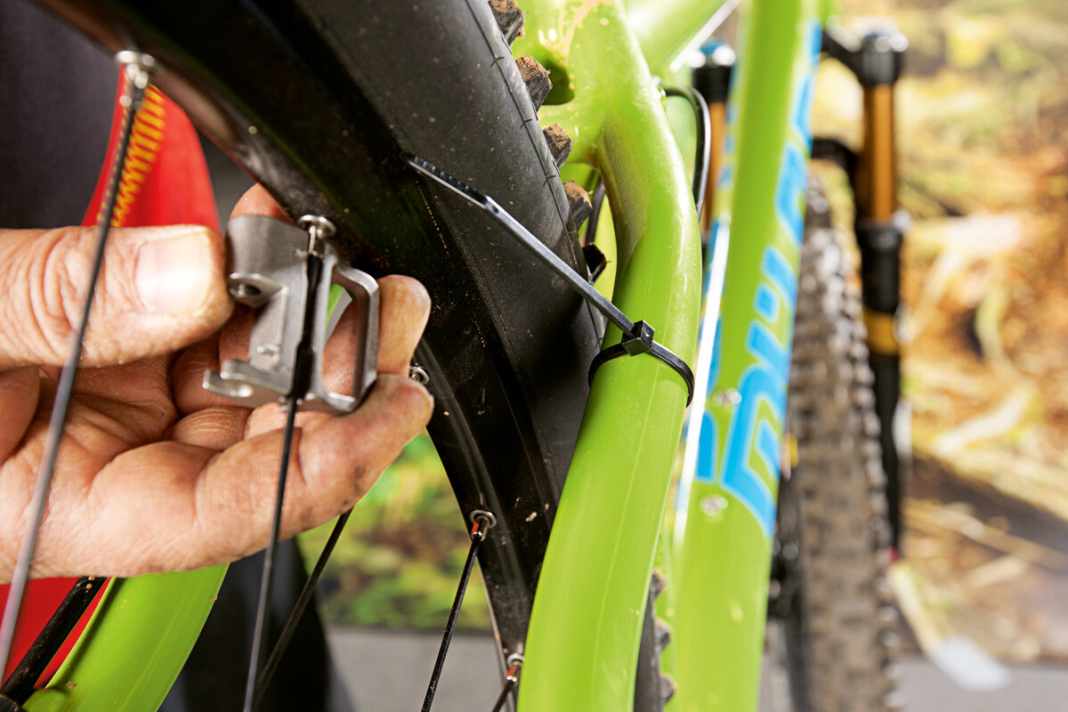 Einen Seitenschlag können Sie auch ohne Zentrierständer notdürftig beheben. Stellen Sie das Bike dazu auf den Kopf. Befestigen Sie einen Kabelbinder an der Kettenstrebe oder Federgabel, so, dass er nicht mehr verrutschen kann. Drehen Sie ihn bis fast an die Felge. Wenn Sie nun das Laufrad langsam drehen, können Sie den Seitenschlag lokalisieren. Gehen Sie beim Anziehen der Speichen schrittweise vor. Ziehen Sie die Speichen, die dem Seitenschlag entgegenwirken im Uhrzeigersinn an. Immer nur eine Viertelumdrehung, danach kontrollieren Sie den Seitenschlag erneut. Solange noch ein Schlag feststellbar ist, müssen Sie wiederholt die Speichen nachspannen. So lange, bis das Laufrad wieder rundläuft.