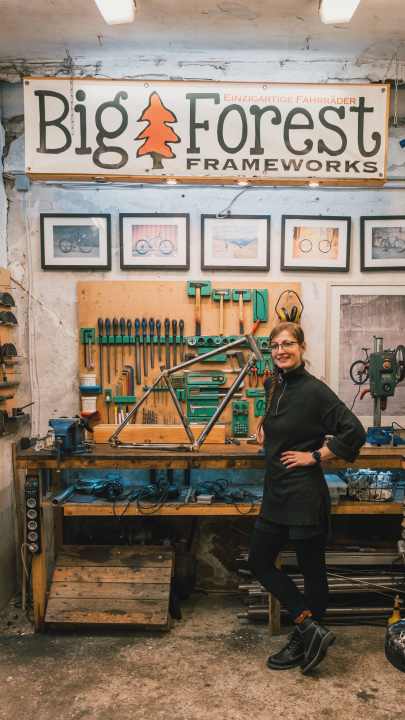Eine stolze Juliane mit ihrem selbstgebauten Gravelbike-Stahlrahmen in der Werkstatt von Big Forest Frameworks.