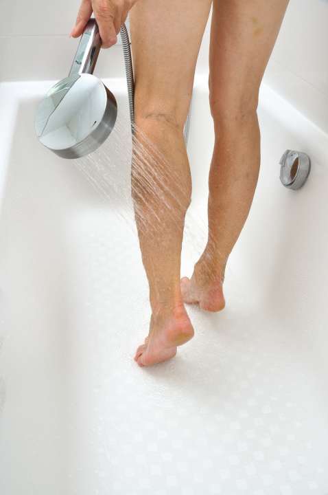 Seniorin spült in der Badewanne ihre Beine ab