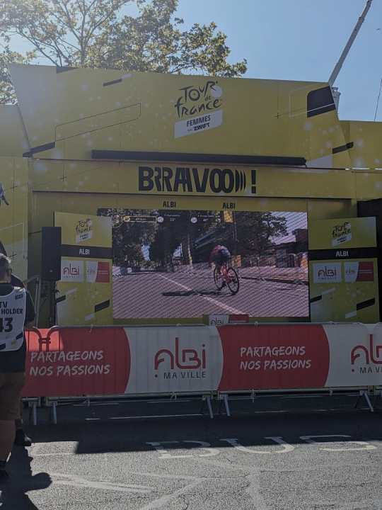 Ricarda Bauerfeind auf der großen Leinwand im Zielbereich. In wenigen Momenten wird sie hier über die Ziellinie fahren und die Etappe gewinnen.