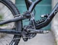 Wie der Name schon sagt, sitzt der Hauptdrehpunkt bei einem High-Pivot-Bike wie dem Norco Range nicht wie gewöhnlich in Tretlagernähe, sondern deutlich weiter oben. Beim Einfedern vergrößert sich so der Abstand zwischen Tretlager und Hinterradachse, wodurch das Hinterrad dem Hindernis nach hinten ausweicht, anstatt daran “hängen” zu bleiben. Der Nachteil: Je größer die Kettenstrebenlängung, desto mehr zieht die Kette das Kettenblatt beim Einfedern zurück. Je nach Kettenzug führt das zu negativen Einflüssen auf das Fahrwerk und zu Pedalrückschlag. Um das Fahrwerk von diesen Antriebsein­flüssen zu entkoppeln, läuft die Kette über eine Umlenkrolle nahe dem Drehpunkt.