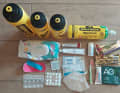 Feuchttücher, Kinesiotape, Desinfektionstücher, Corona-Schnelltest, FFP2-Maske, Sonnencreme, Zahnbürste, Zahnpasta, Riegel, Nahrungsergänzungsmittel, 2 Flaschen 0,75 Liter, 1 Flasche 1 Liter, Wasseraufbereitungstabletten, Magentabletten, Salztabletten, Koffeintabletten, Chamois Creme