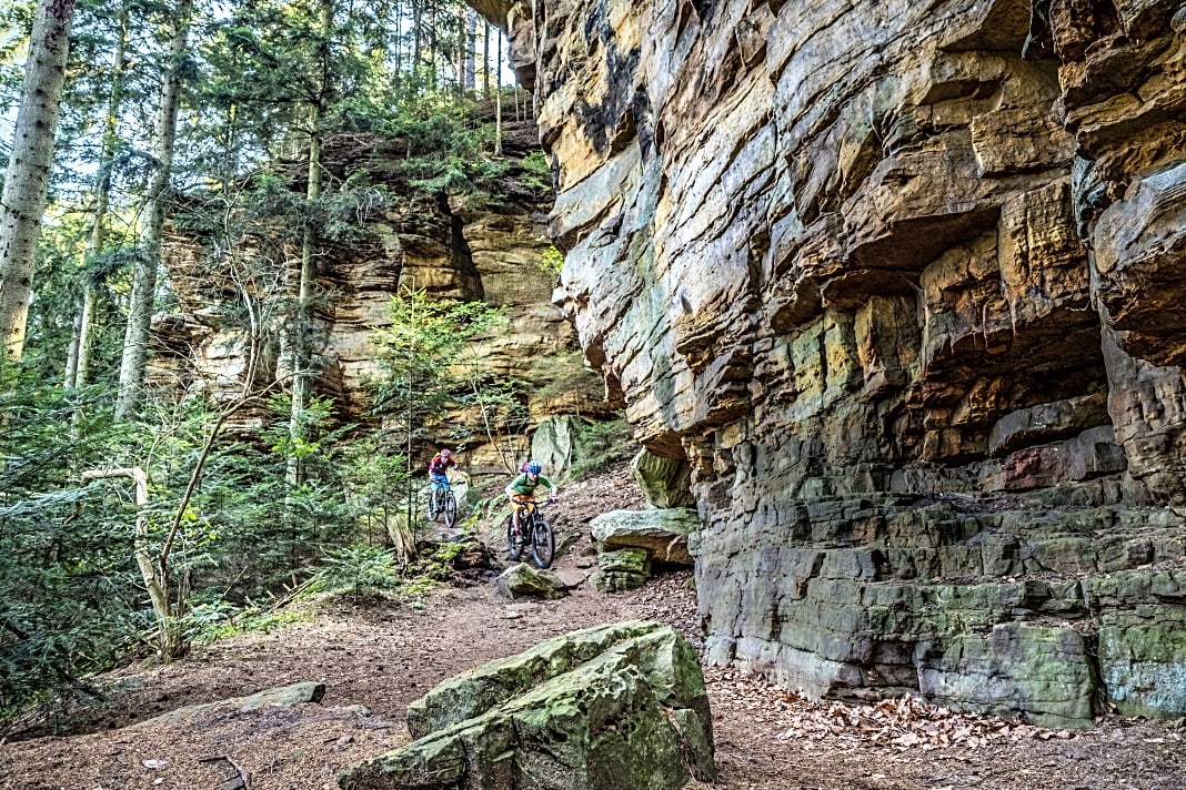 Auf dem Singletrail im Mullerthal. Ein schmaler Felsenpfad führt am Steilhang entlang des Sauertals in Richtung Berdorf. Für gute Biker ist der Trail leicht befahrbar, für Anfänger grenzwertig, da schmal, teilweise ausgesetzt und mit Steinen und Felsbrocken übersät.