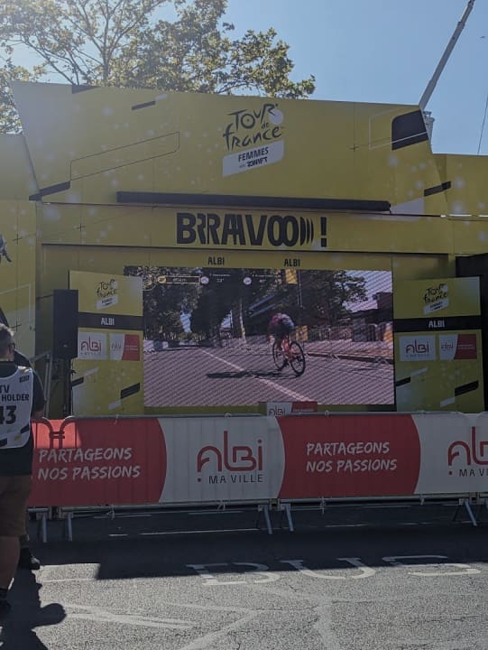 Ricarda Bauerfeind auf der großen Leinwand im Zielbereich. In wenigen Momenten wird sie hier über die Ziellinie fahren und die Etappe gewinnen.