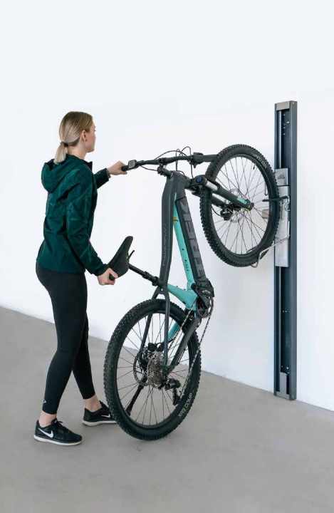 Wandhalter mit eingebautem Lift schonen nicht nur Rücken und Handgelenke, sondern auch das Rad selbst. Der silberne Schlitten im mechanischen Halter von Biohort für 399 Euro (>> <a href="https://www.awin1.com/cread.php?awinmid=9326&awinaffid=471469&clickref=B+Biohort+Bikelift&ued=https%3A%2F%2Fwww.obi.de%2Fp%2F1928597%2Fbiohort-bikelift-wandmontage-schwenkbar-fuer-gartenhaus-16x53x182-cm-dunkelgrau" target="_blank" rel="noopener noreferrer nofollow">hier erhältlich</a>*) aufwärts nimmt das Rad auf beiden Reifen stehend auf und hilft mit Federkraft, das Bike in aufrechte Position zu ziehen. Solche Lifte gibt’s auch mit Elektromotor, neben der nötigen Verkabelung stört hier aber oft die lange Dauer, bis das Bike verstaut oder abgelassen ist.